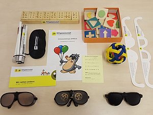 AM4Kids-Lernbox bestehend aus Langstock, Augenbinden, Simulationsbrillen, Braille-Alphabet und haptischen Holzbausteinen