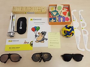 AM4Kids-Lernbox bestehend aus Langstock, Augenbinden, Simulationsbrillen, Braille-Alphabet und haptischen Holzbausteinen