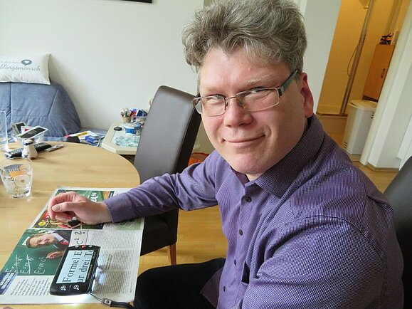 Peter G. sitzt an einem Tisch mit einer elektronischen Lupe.