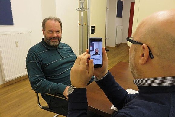 Mitarbeiter Daniele Marano fotografiert mit seinem Smartphone einen Mann mit Bart.“