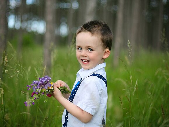 Emil steht mit einem kleinen Blumenstrauß in der Wiese