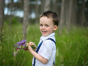 Emil hilft seiner hochgradig sehbehinderten Schwester Lisa oft und gerne. Emil steht mit einem kleinen Blumenstrauß in der Wiese