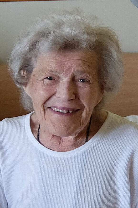 Eine ältere Dame mit weißer Dauerwelle lächelt freundlich in die Kamera
