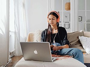 Eine junge Frau sitzt vor einem Laptop. Sie hat Kopfhörer aufgesetzt.