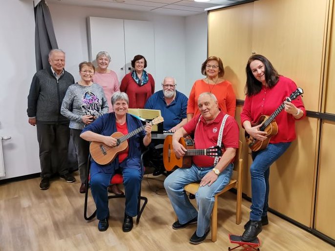 Acht Mitglieder der Singgruppe der Hilfsgemeinschaft spielen auf ihren Instrumenten und singen bei einer Probe.