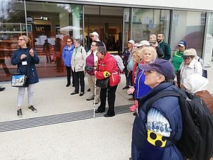 17 Personen stehen vor dem verglasten Museumsgebäude.