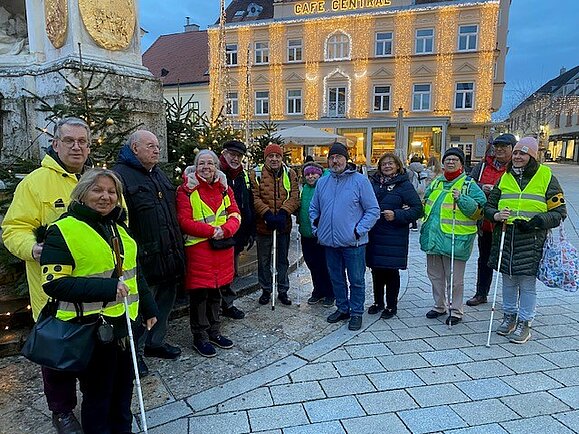 Mehrere Personen, teilweise mit Armschleife oder Taststock, stehen auf einem adventlich geschmückten Platz