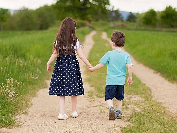Sehsternchen Lisa und Bruder Emil gehen Hand in Hand einen Feldweg entlang.