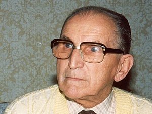 Foto eines älteren Herren mit großer Brille und Krawatte. 