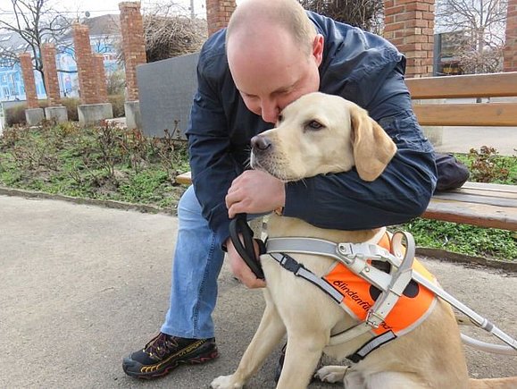 Alexander S. kuschelt auf einer Parkbank mit seinem Blindenführhund Flint