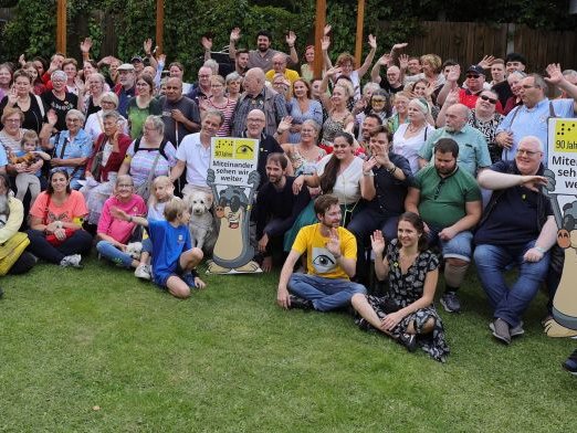 Gute Laune bei der Jubiläumsfeier Ein Gruppenfoto von vielen Menschen mit dem Maskottchen AUGust