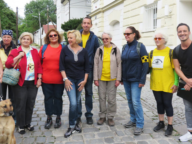 Fröhliche Mitglieder der Hilfsgemeinschaft in Wanderkleidung stehen nebeneinander wartend am Treffpunkt