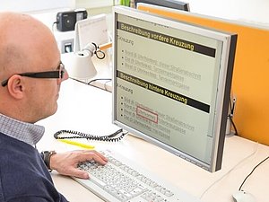 Ein Mann mit Brille sitzt vor einem Computer und schaut sich eine Website, die er sich vergrößert hat, an.