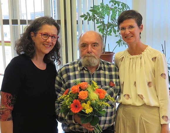 Zwei Frauen mit älterem Herrn mit Blumenstrauß in der Hand