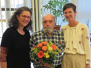 Zwei Frauen mit älterem Herrn mit Blumenstrauß in der Hand