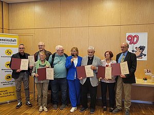 Mehrere Personen stehen nebeninander und halten eine Urkunde in der Hand. In der Mitte steht eine Frau die moderiert und der Vorstandsvorsitzende Fürst