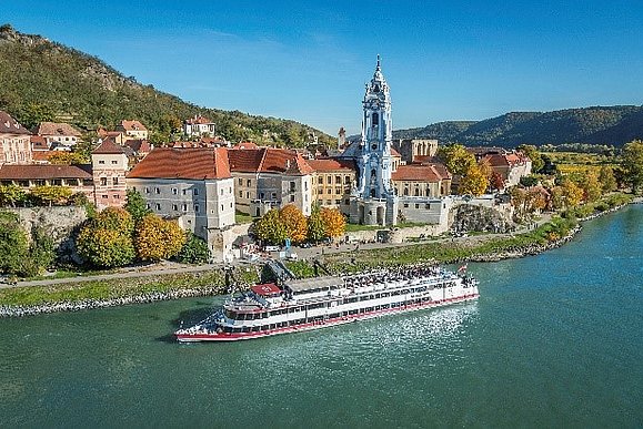 Die Wachau ist UNESCO Welterbe. Stadt an der Donau mit Kirchturm, großes Schiff fährt vorbei
