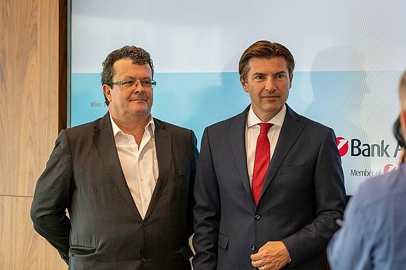 Zwei Männer in Anzügen posieren gemeinsam für ein Foto.