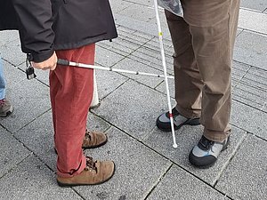 Mann mit weißem Stock spricht mit Frau mit weißem Stock und Augenbinde