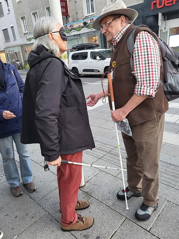 Mann mit weißem Stock spricht mit Frau mit weißem Stock und Augenbinde