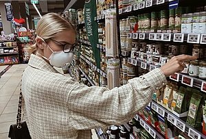 Eine Frau mit Mund-Nasen-Schutz steht vor einem Supermarktregal.