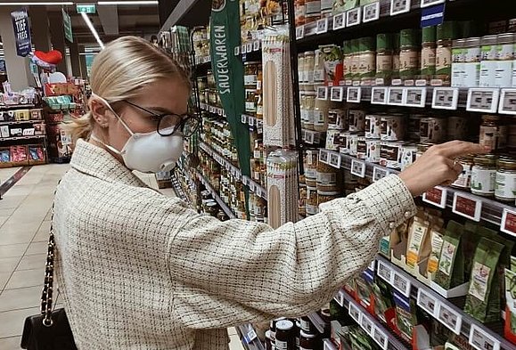 Julia kauft für unser Mitglied Johanna ein. Eine Frau mit Mund-Nasen-Schutz steht vor einem Supermarktregal.