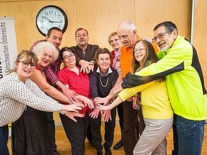 Mehrere Menschen stehen in einem Halbkreis und strecken die Hände alle in die Mitte.