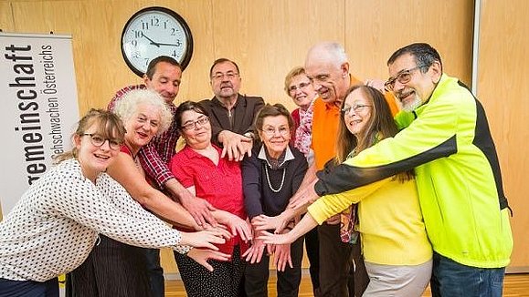 Mehrere Menschen stehen in einem Halbkreis und strecken die Hände alle in die Mitte.