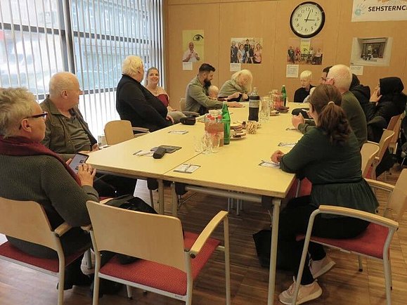 Personen sitzen an großem Tisch und plaudern.