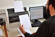 Mann von hinten schaut sich Brailledruck an vor einem Drucker