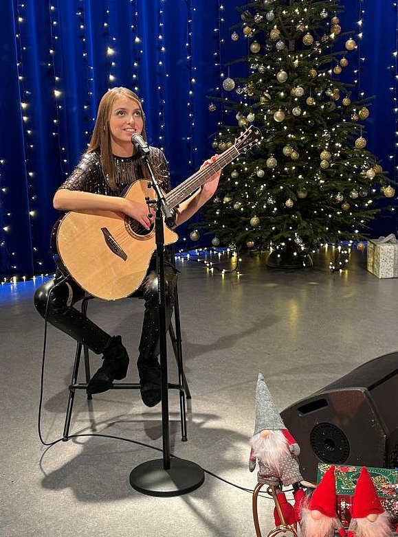 Eine junge Frau mit dunklen Haaren spielt Gitarre, im Hintergrund ein Weihnachtsaum