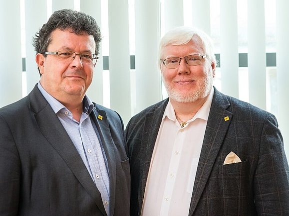 Zwei Männer im dunklen Anzug stehen nebeneinander.