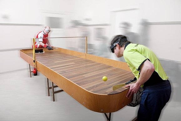 Showdown-Tisch und zwei Spieler mit Augenbinden, Handschuhen und Schlägern ausgestattet, spielen den Ball.