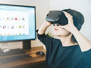 Junger Bub mit VR-Brille sitzt am Schreibtisch mit PC schaut nach oben