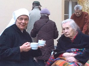 Nonne mit Teetasse in der Hand und ältere Dame mit Decke schauen in die Kamera