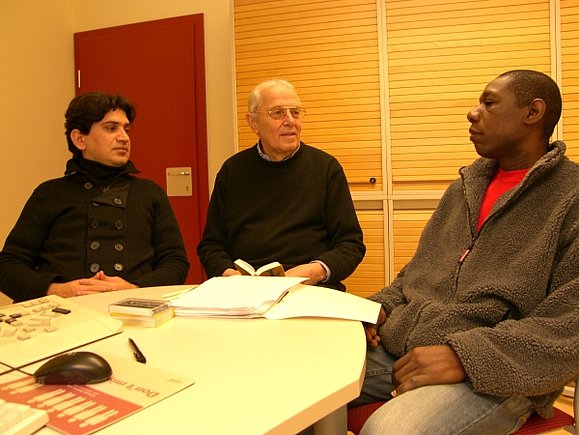 Heinz Natorski mit zwei seiner Schüler. 3 Männer sitzen rund um einen Tisch. Am Tisch liegen Lernunterlagen, ein Mann hat ein Wörterbuch in der Hand.