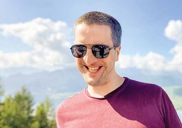 lachender Mann mit Sonnenbrille und purpur Shirt vor blauem Himmel