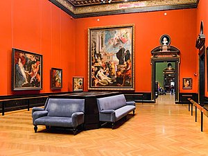Roter barocker Museumssaal mit Couches in der Mitte und Gemälden an der Wand
