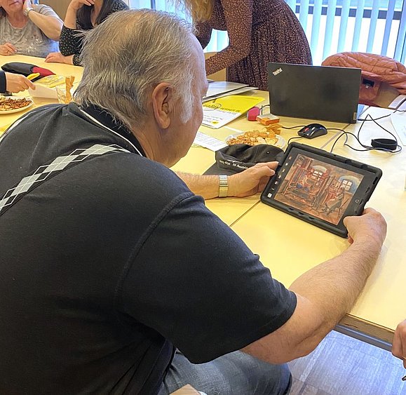 älterer Mann von hinten wie er sich ein Gemälde auf dem Tablet anschaut