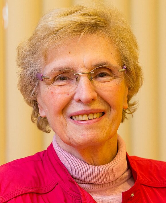 Foto von einer lächelnden alten Frau mit Brillen und rotem Obertiel.