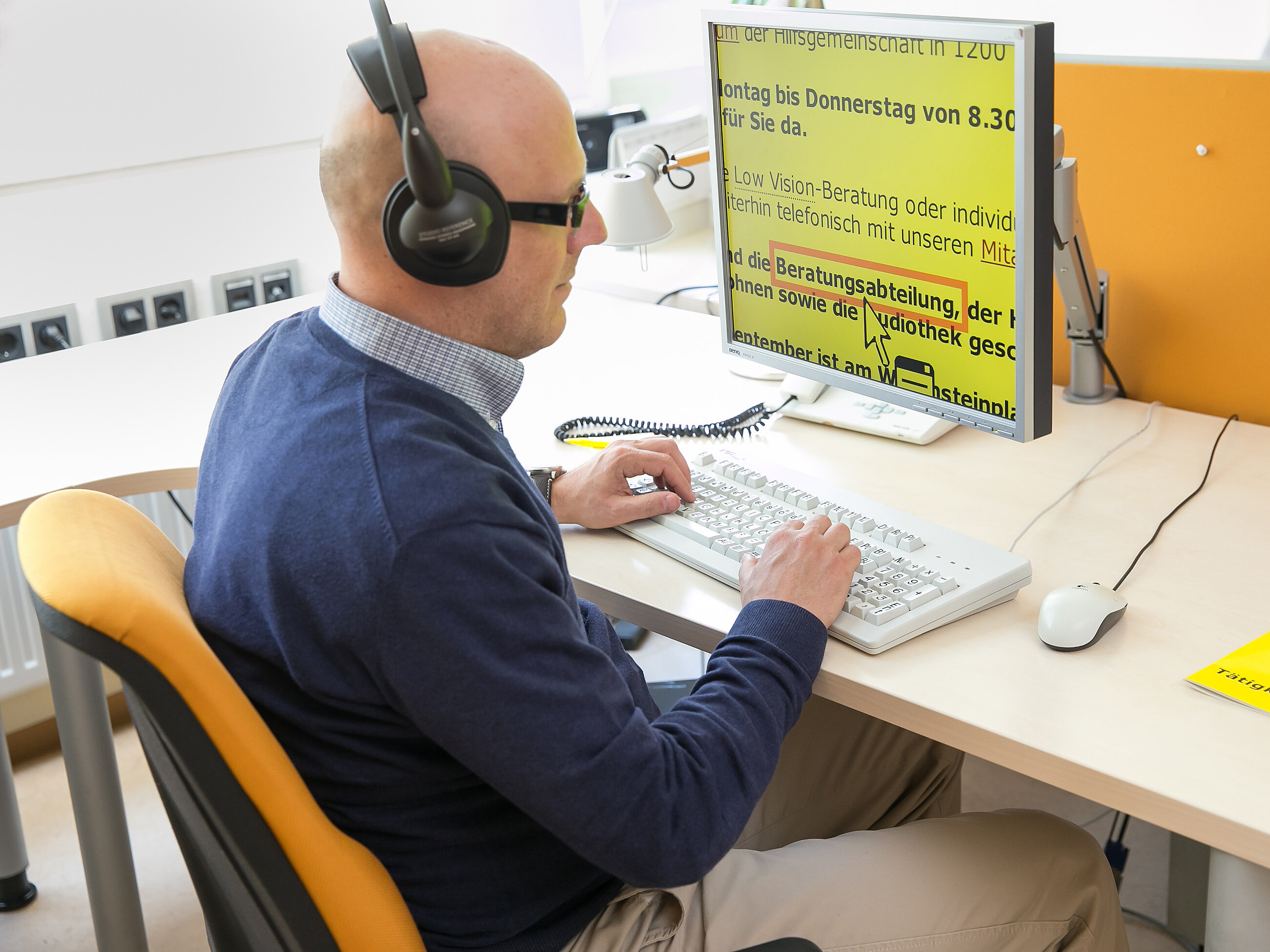 Eine blinde Person sitzt an einem Arbeitsplatz vor einem Bildschirm
