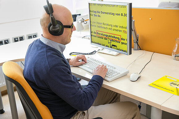 Eine blinde Person sitzt an einem Arbeitsplatz vor einem Bildschirm