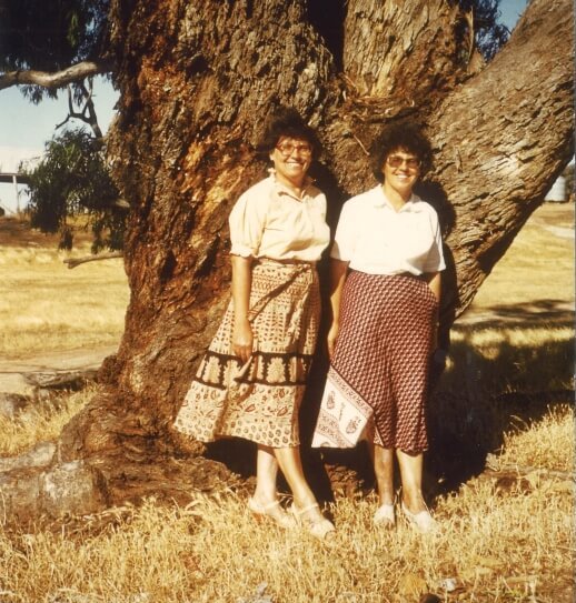 Zwei junge Frauen stehen nebeneinander vor einem großen Baum.