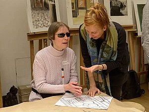 Eine blinde Teilnehmerin testet den taktilen Orientierungsplan während sie mit einer KHM-Mitarbeiterin spricht