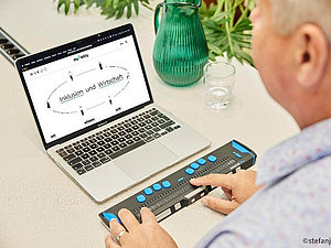 Mann von hinten bedient Laptop mit Braillezeile