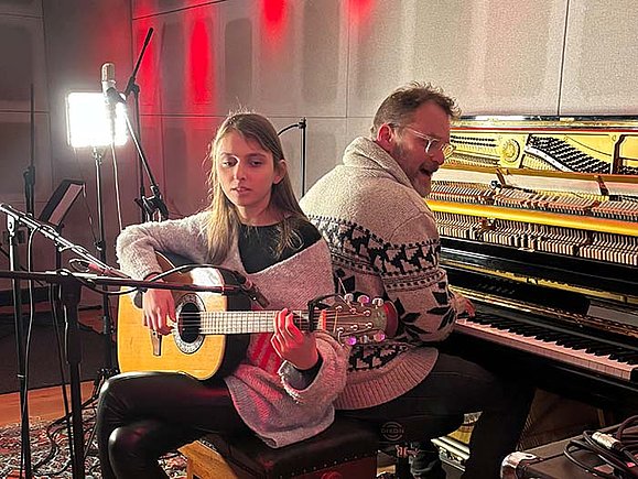 Sofia Reyna und Jerry Meehan im Studio. Foto: Bettina Lichtenwörther Eine junge Frau die Gitarre spielt sitzt Rücken an Rücken mit einem Mann, der eine elektronischen Orgel spielt, in einem Tonstudio.