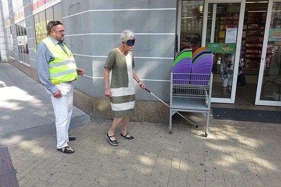 Verkaufsstand steht vor der Türe, Frau bleibt mit Langstock hängen.