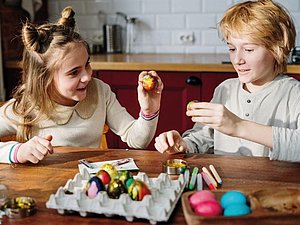 Ein Mädchen und ein Bub haben Spaß beim Bemalen von Ostereiern.