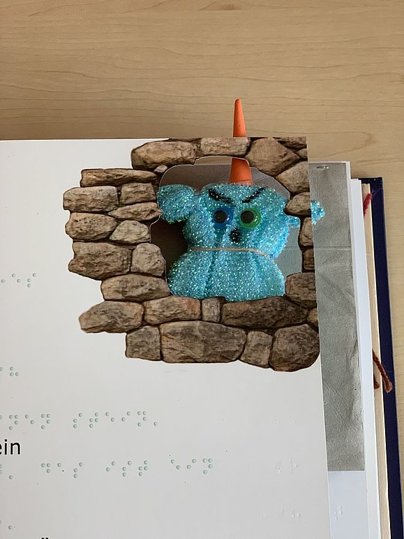 Blaues Glitzermonster mit Horn schaut aus Lochlücke im Buch