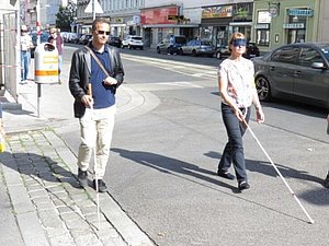 Mann und Frau mit Langstock überqueren eine Straße